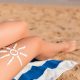 Sun cream is drawn in sun shape on tanned woman's leg who is relaxing on the towel at the beach. Cancer care concept