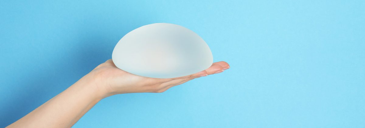 Woman holding silicone implant for breast augmentation on color