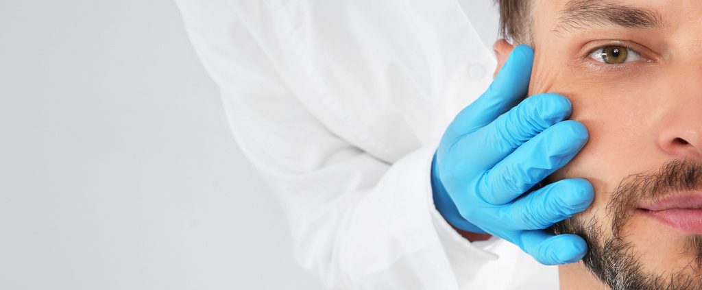 Doctor examining mature man face before cosmetic surgery on white background, closeup